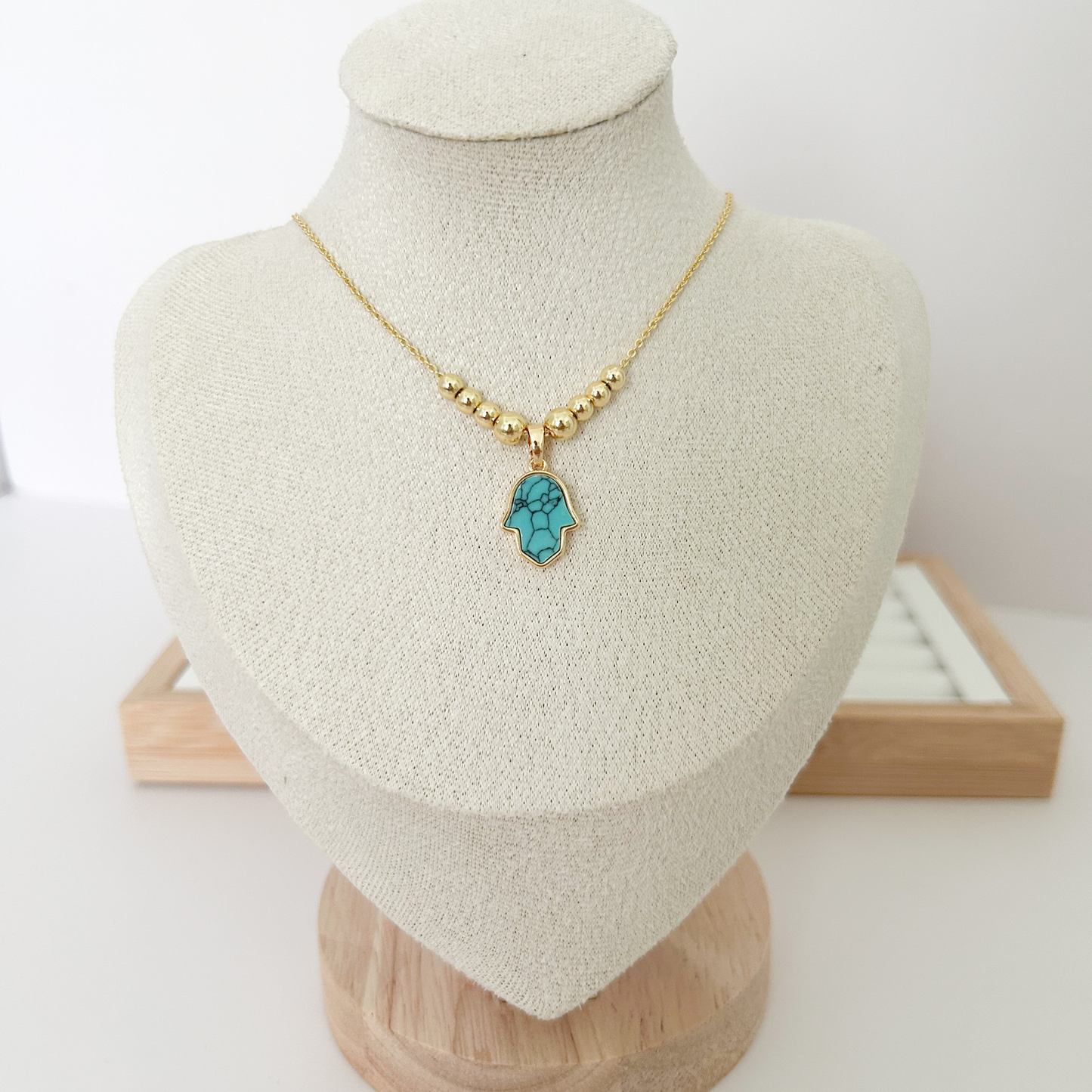 Gold beaded necklace with turquoise Hamsa hand pendant on linen jewelry bust — Citrika