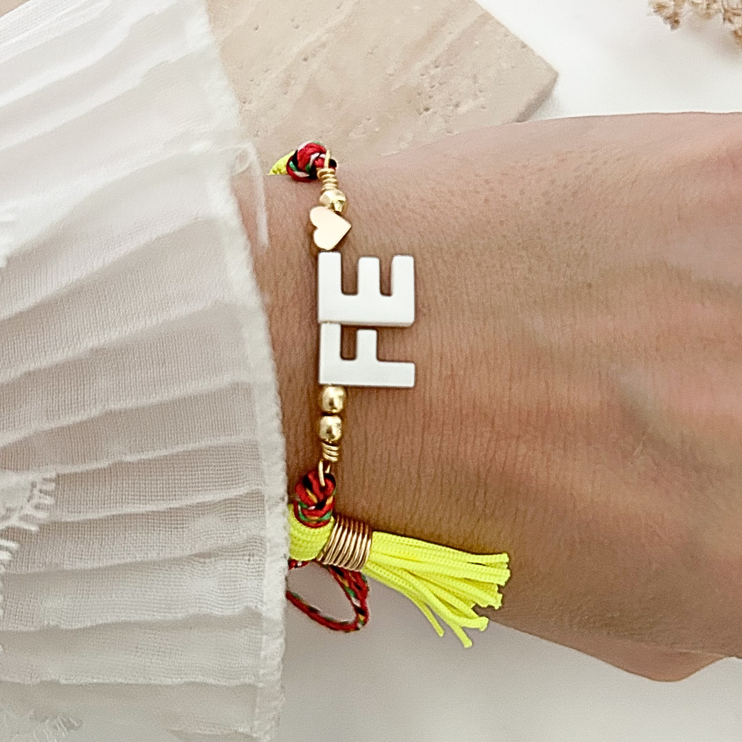 Adjustable faith bracelet featuring bold white “FE” letters, gold-tone accents, colorful braided cords, and a neon yellow tassel, styled on the wrist.