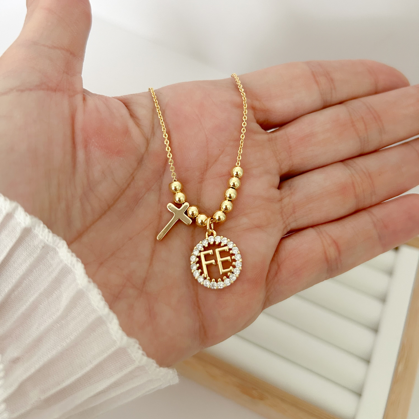 Gold necklace with charms on a hand against a white background