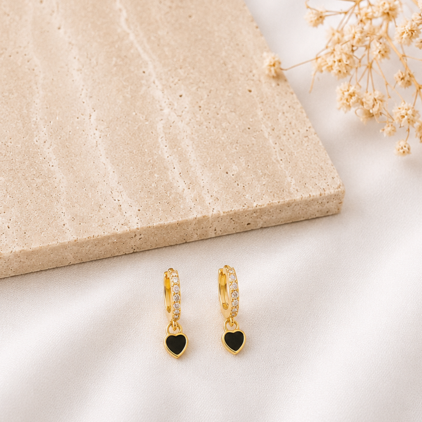 Pair of gold-tone huggie hoop earrings with pavé cubic zirconia accents and dangling black enamel heart charms. Minimalist heart earrings with a timeless design, perfect for everyday wear or layering with other gold jewelry.