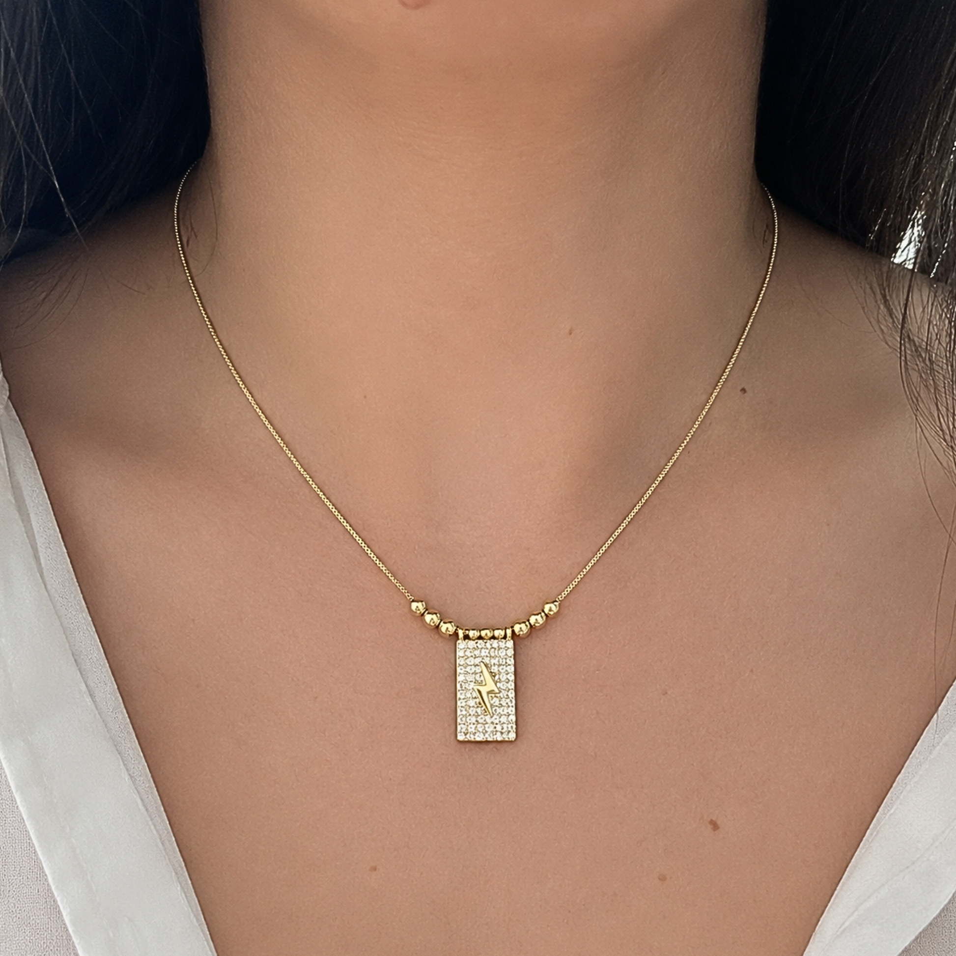 Minimalist gold necklace worn on a model, featuring a shimmering rectangular pendant with a bold lightning bolt centerpiece.