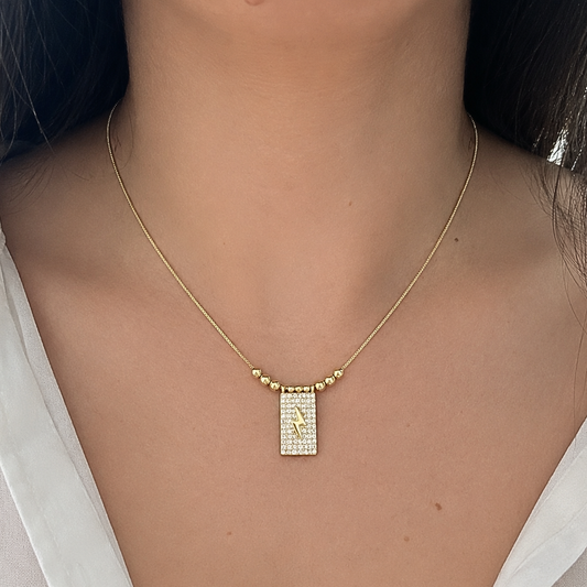 Minimalist gold necklace worn on a model, featuring a shimmering rectangular pendant with a bold lightning bolt centerpiece.