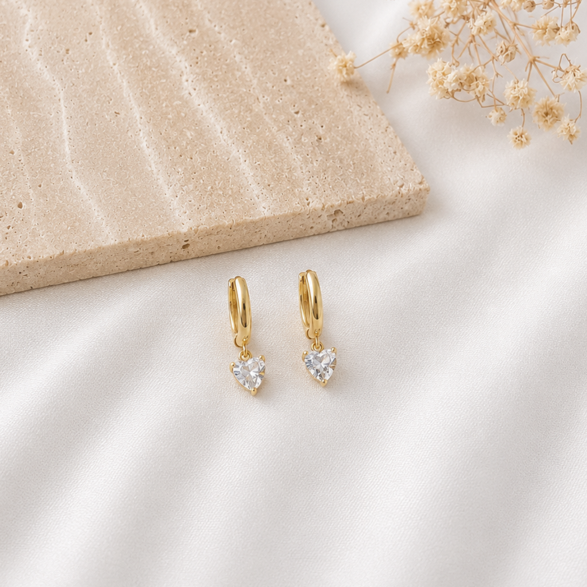 Pair of minimalist gold-tone huggie hoop earrings with dangling heart-shaped clear cubic zirconia charms. Delicate heart drop earrings with a polished gold finish, perfect for everyday wear, layering, romantic gifts, or special occasions.