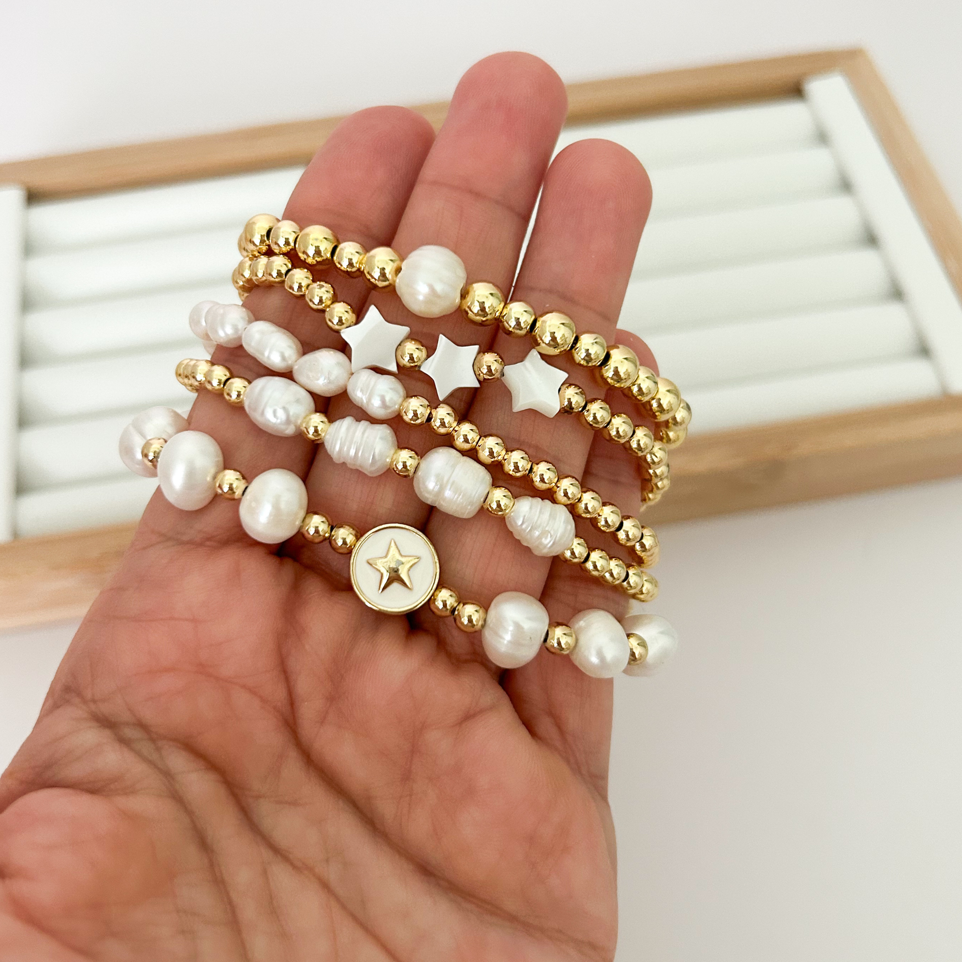Five gold bracelets with freshwater pearls and star charms held in hand