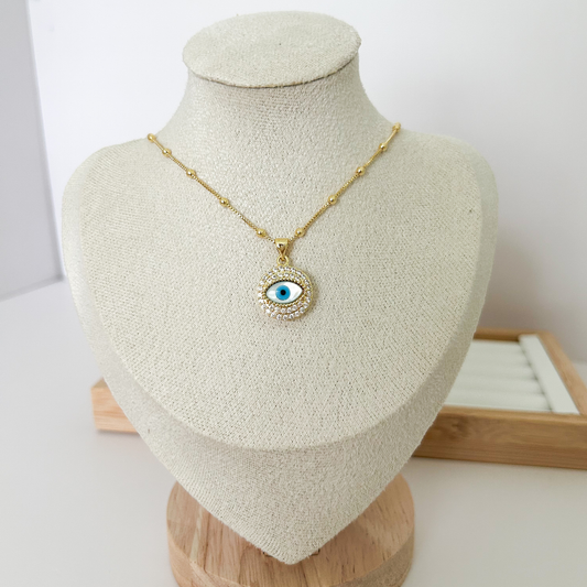 Gold evil eye pendant necklace with blue enamel and zirconia halo on gold chain on white background — Citrika