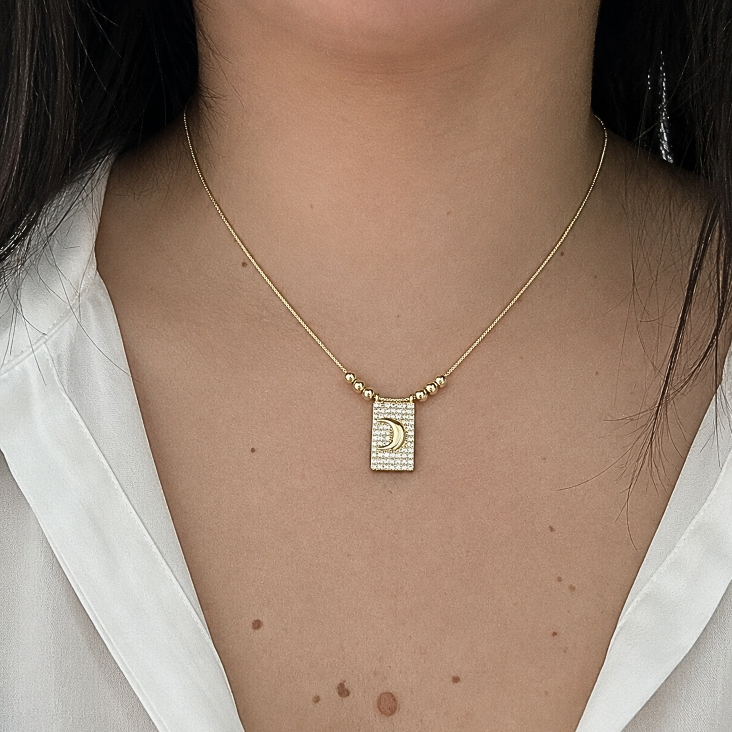 Elegant gold-tone necklace worn on a model, featuring a crystal-studded rectangular pendant with a polished crescent moon centerpiece.