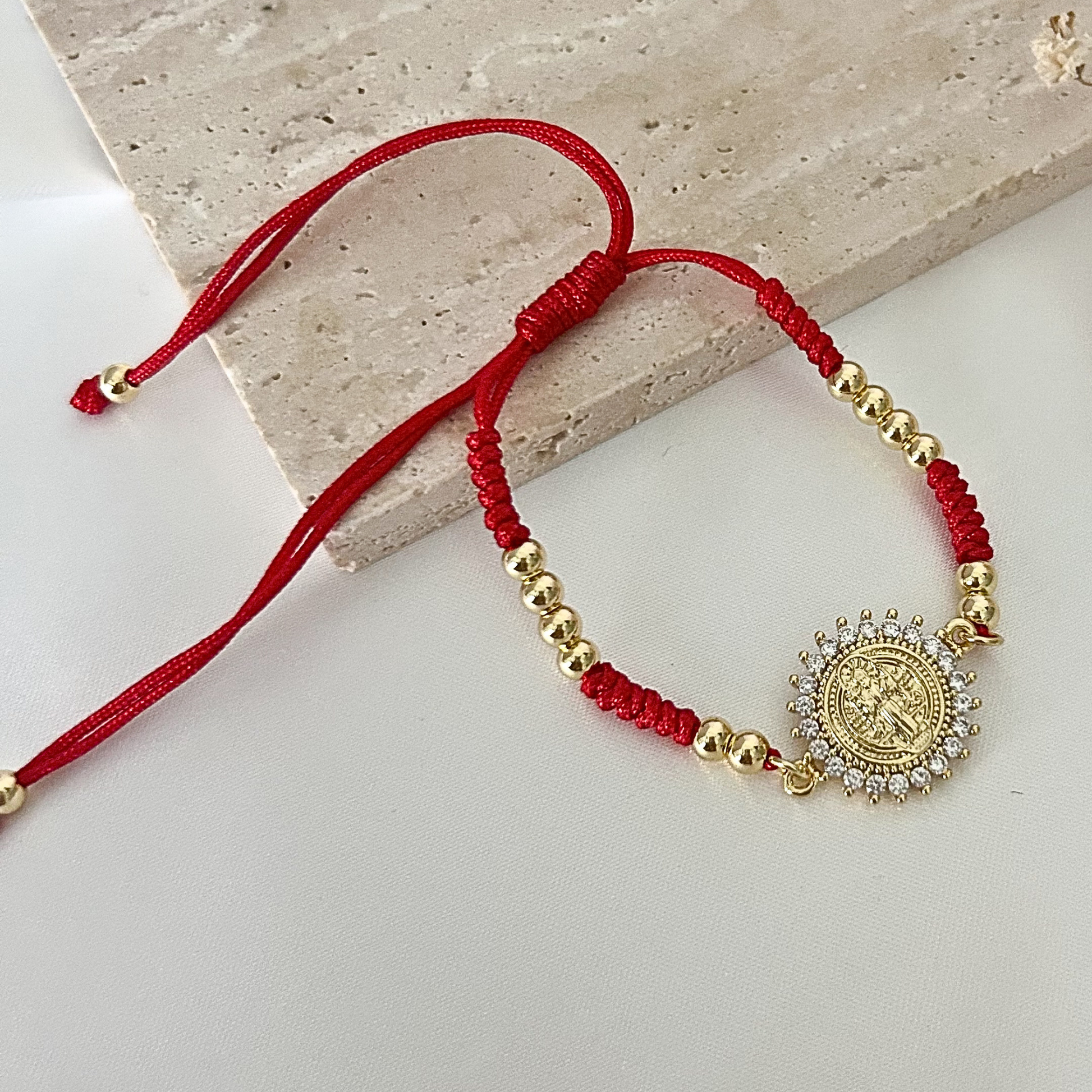 Red adjustable bracelet featuring a sparkling Saint Benedict medallion framed with clear crystals and accented with gold-tone beads.