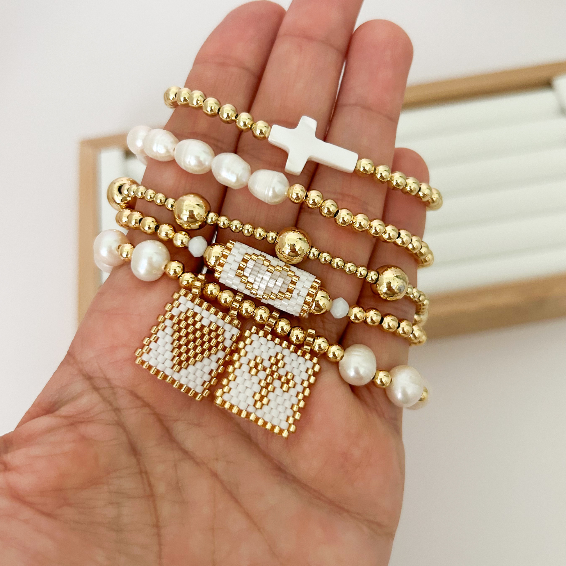 Five gold bracelets with miyuki weave and mother of pearl cross held in hand