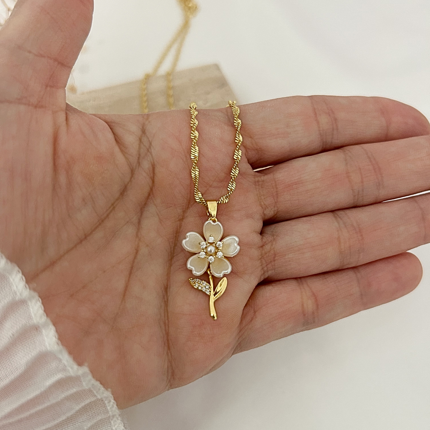 Gold flower pendant necklace with mother-of-pearl petals, pearl center, and cubic zirconia accents, shown in hand to highlight its elegant size and delicate craftsmanship.