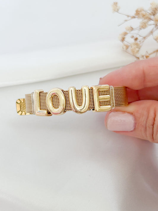 Gold 'LOVE' bracelet held by a hand on a light background