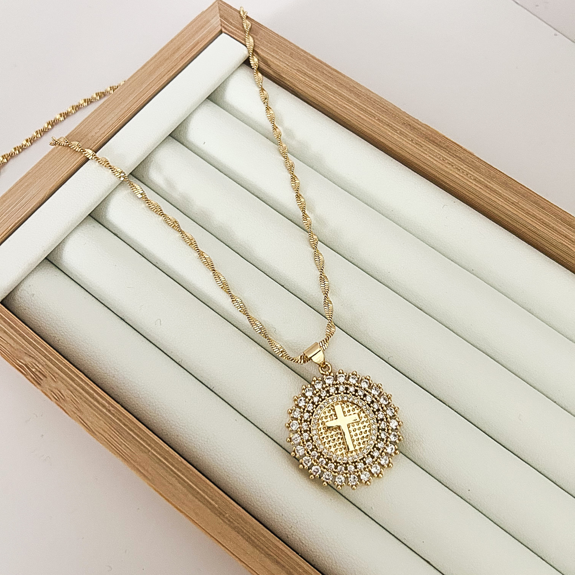 Gold faith necklace with round cross pendant on neutral jewelry tray.