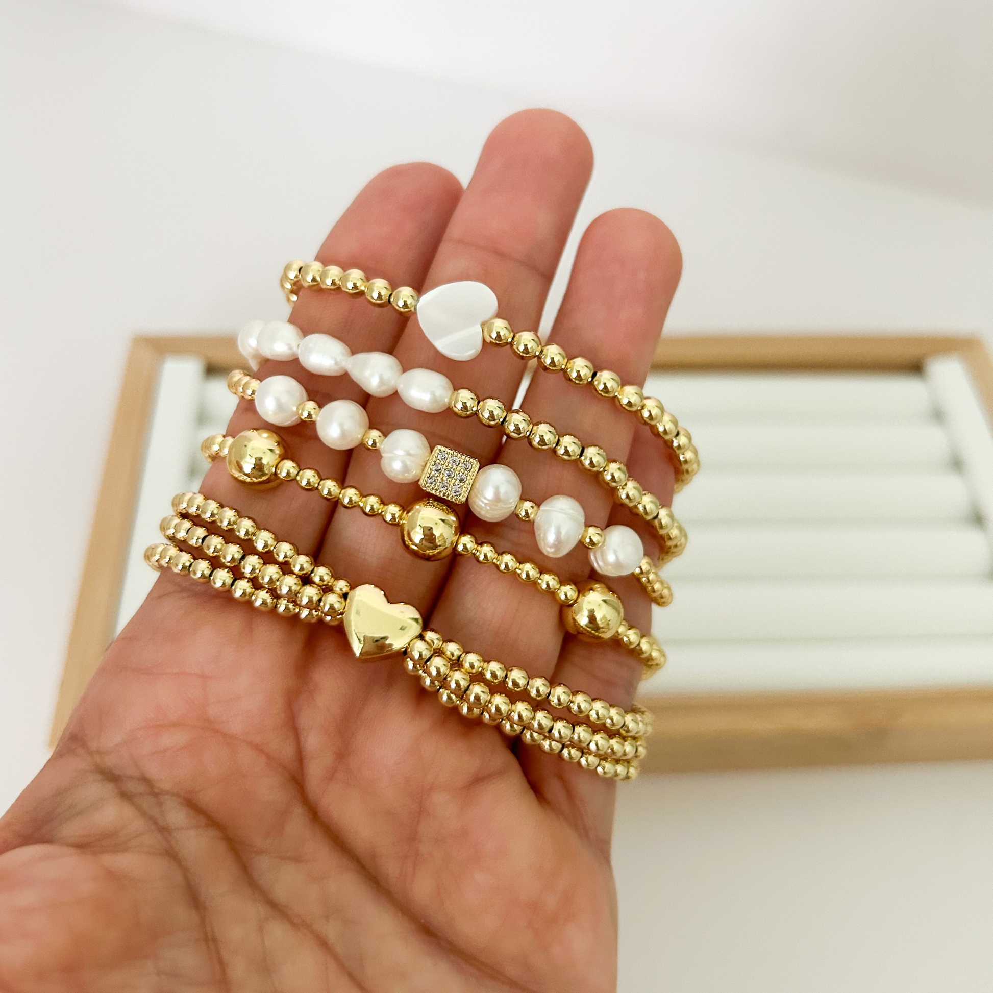 Five gold bracelets with freshwater pearls and gold heart charm held in hand
