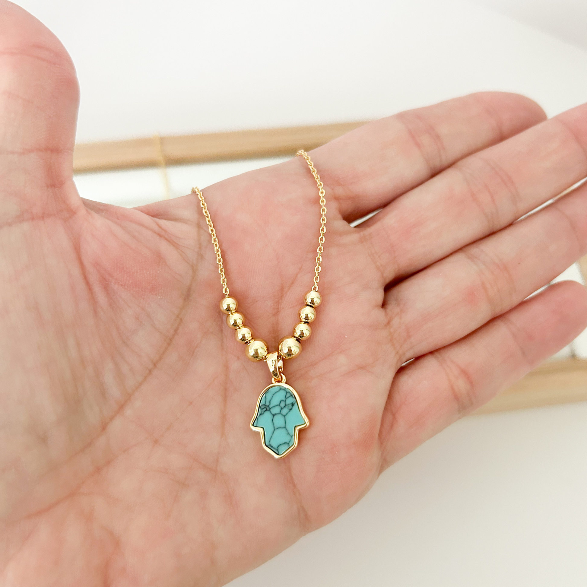 Gold beaded necklace with turquoise Hamsa hand pendant on linen jewelry bust — Citrika