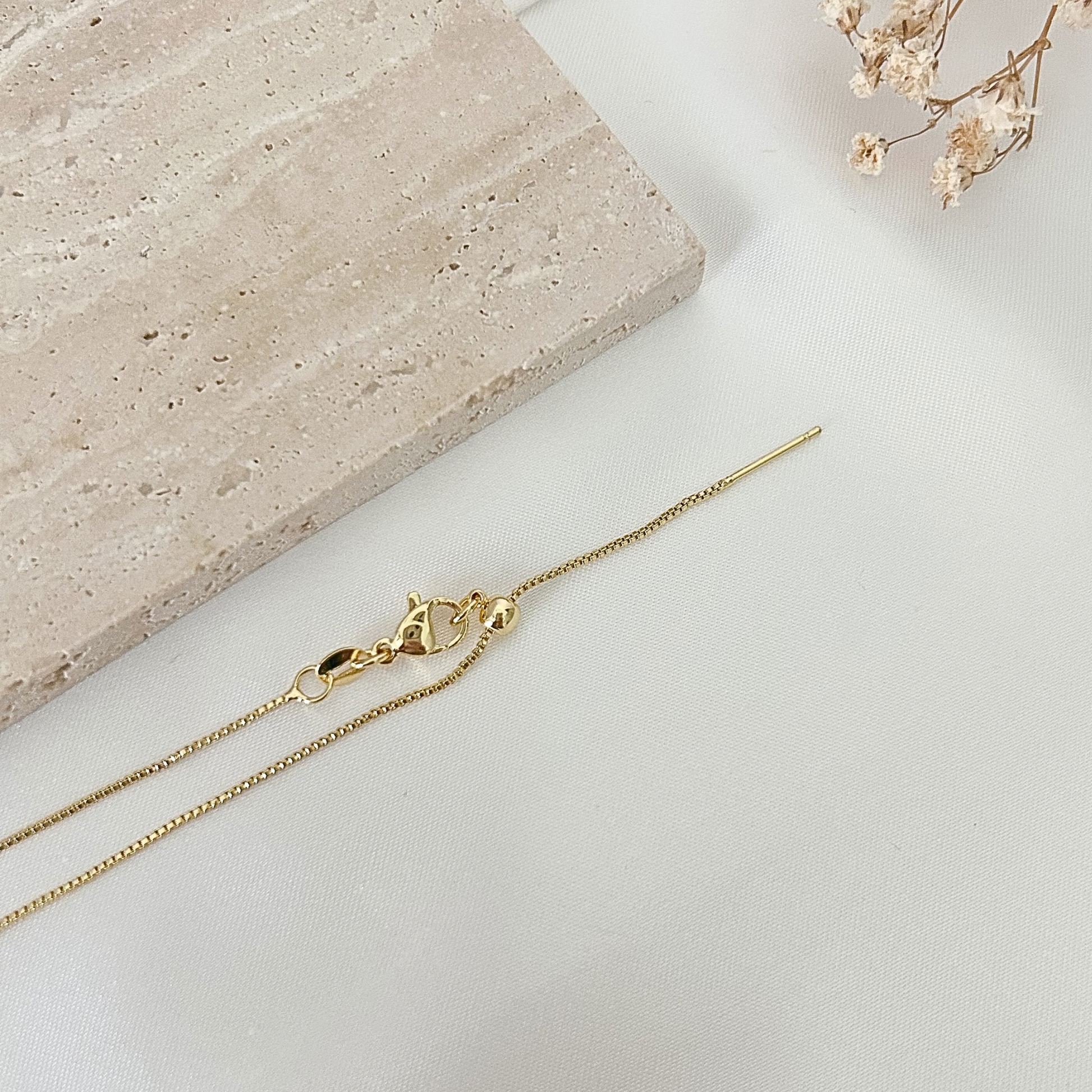 Adjustable gold necklace with a sliding clasp closure and moon pendant, photographed against a soft neutral background for a minimalist jewelry presentation.