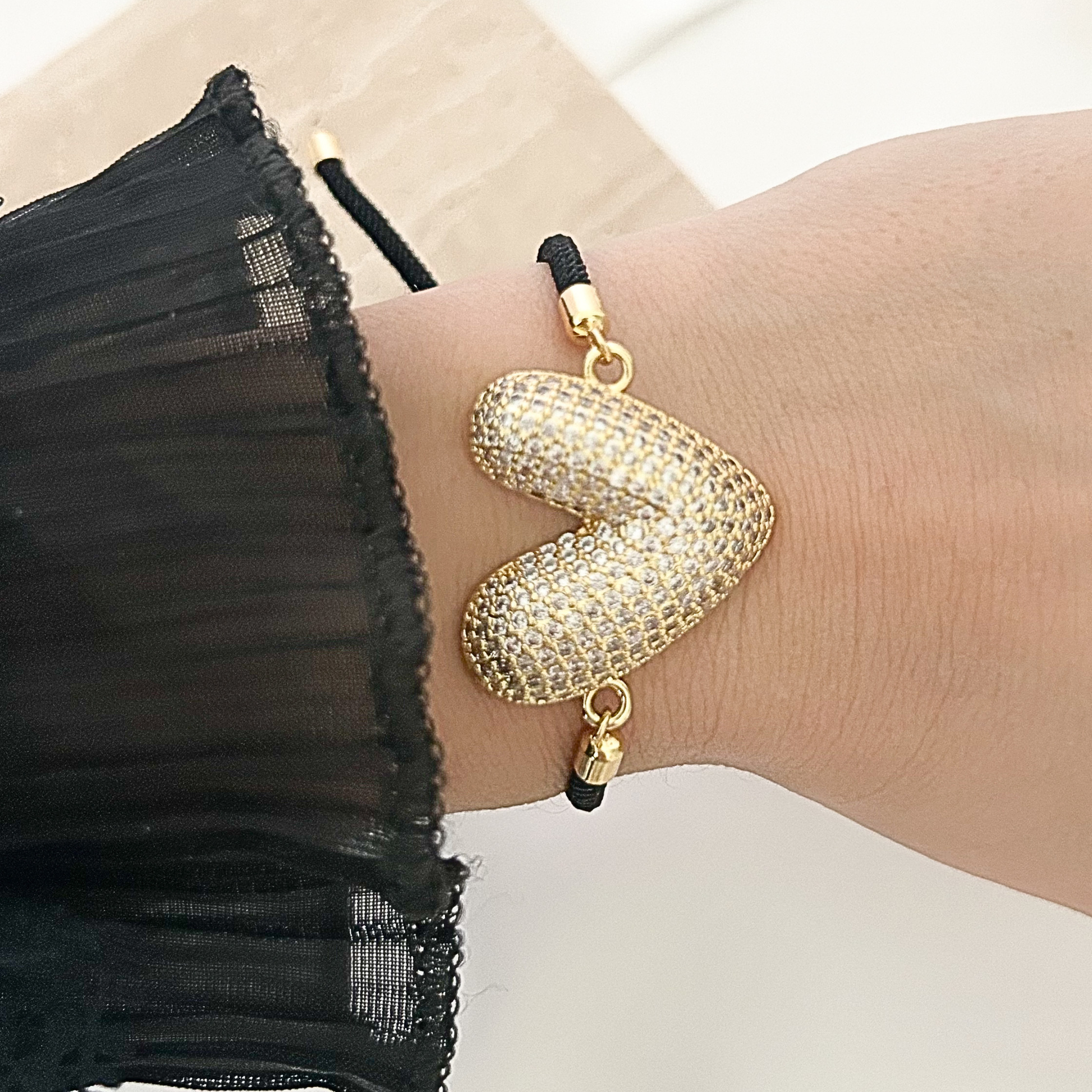 Statement bracelet featuring a large crystal-encrusted heart charm in gold-tone metal attached to a sleek black adjustable cord.