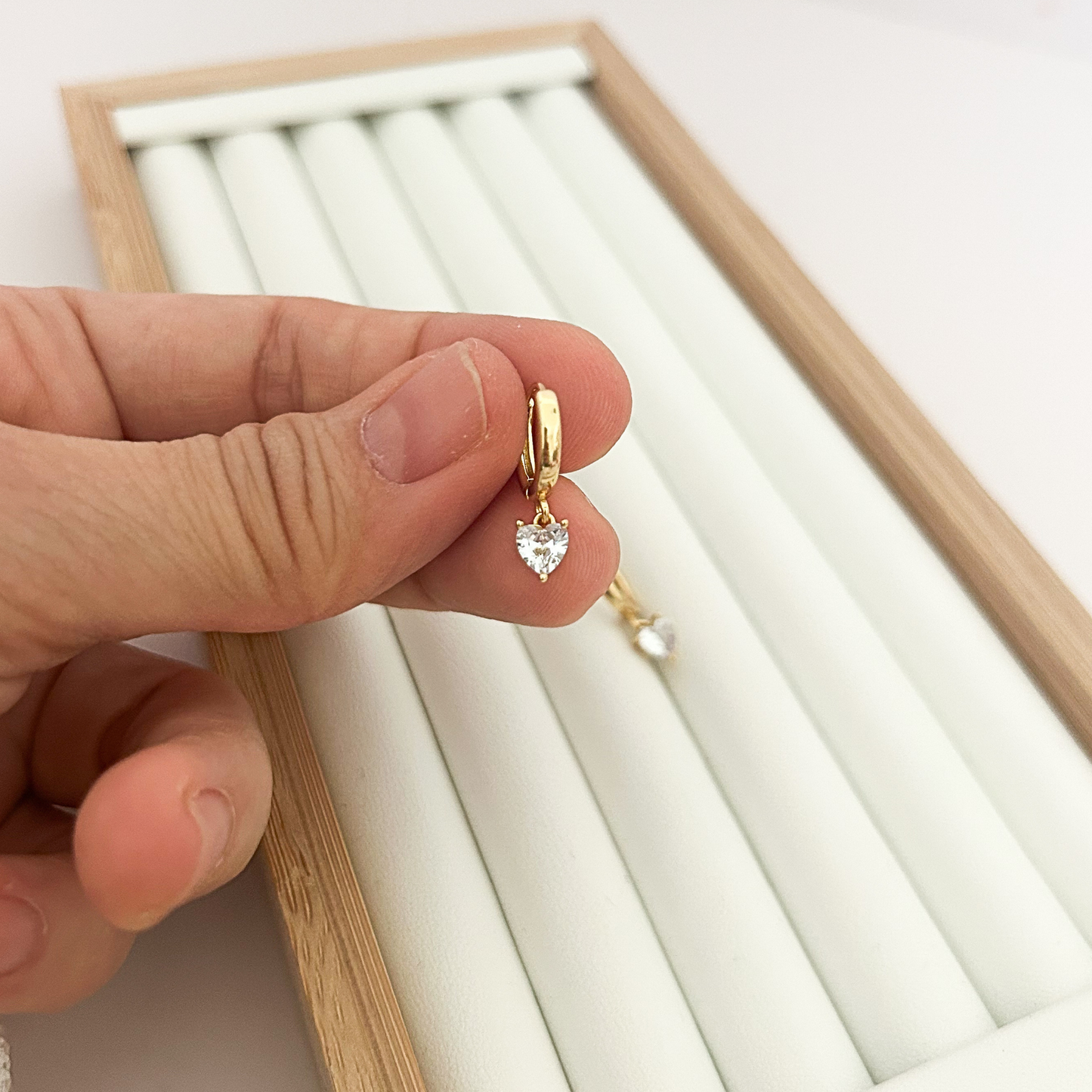 18K gold plated hoop earring with cubic zirconia heart charm held in hand — close-up