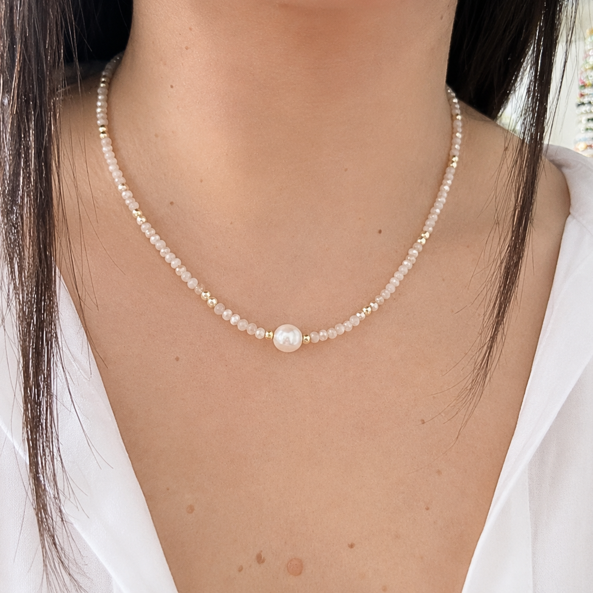 Elegant blush pink beaded necklace featuring a freshwater pearl centerpiece and gold-tone accents, worn on a model for a delicate, feminine look.