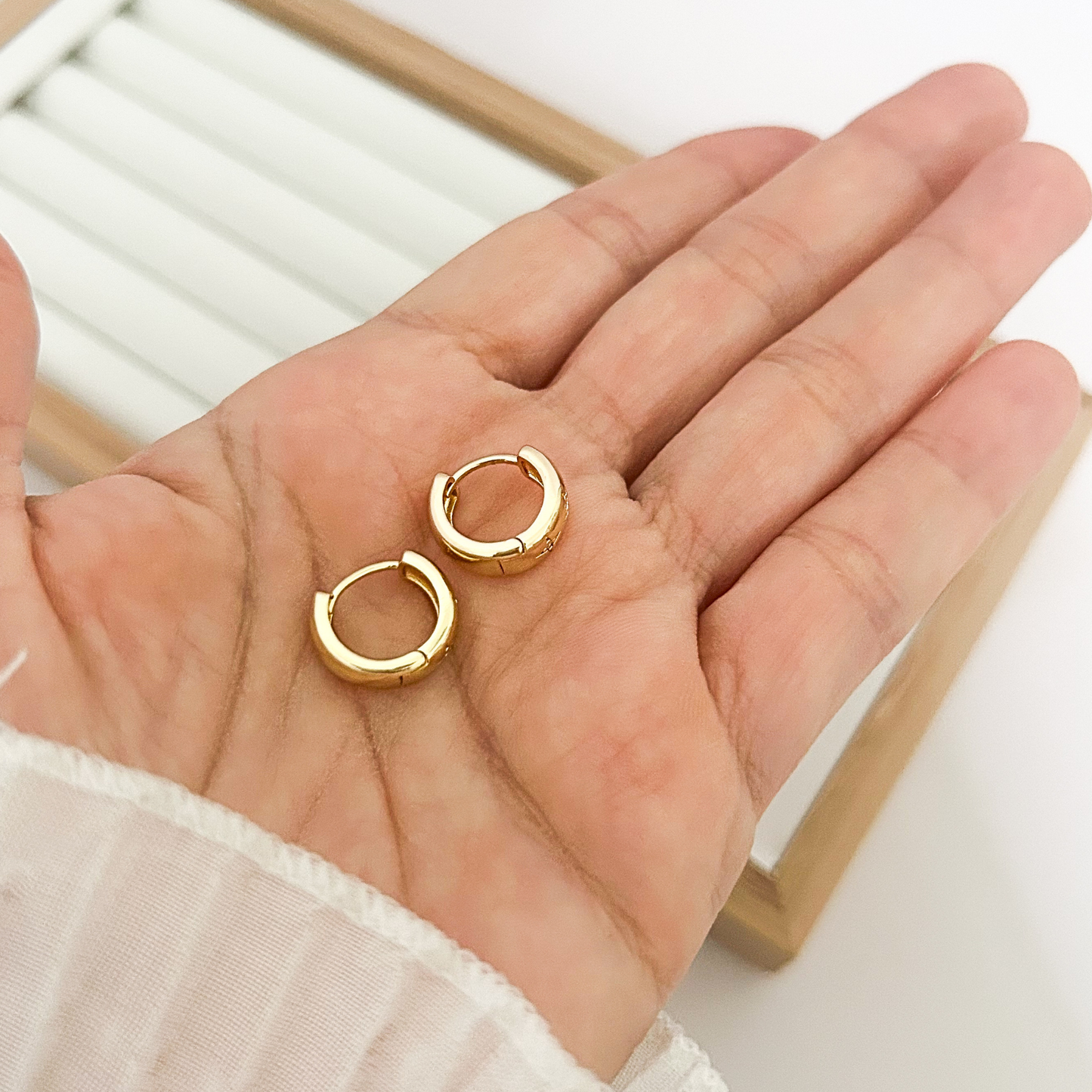 Pair of mini gold huggie hoop earrings held in open palm