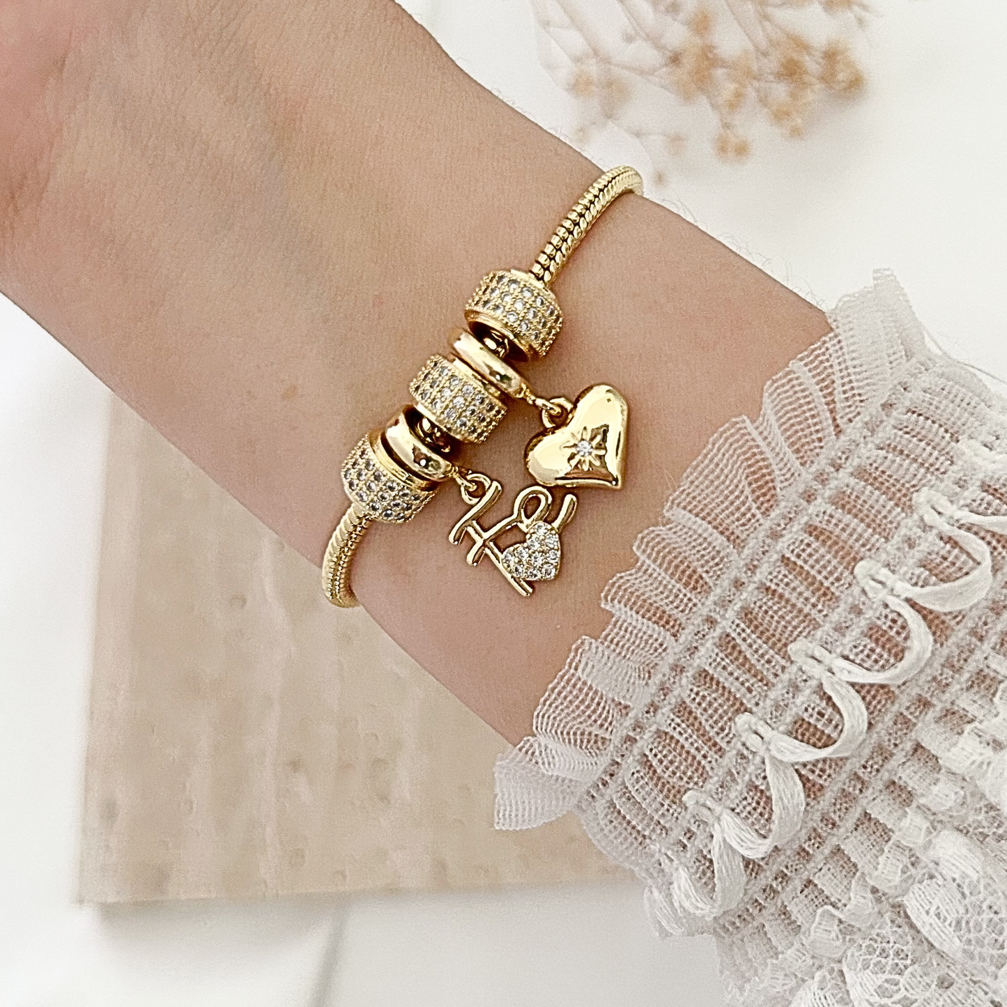 Gold-tone charm bracelet with sparkling crystal spacers, a dangling heart charm, and a “Hope” charm accented with crystals, styled on the wrist with a delicate white lace sleeve.