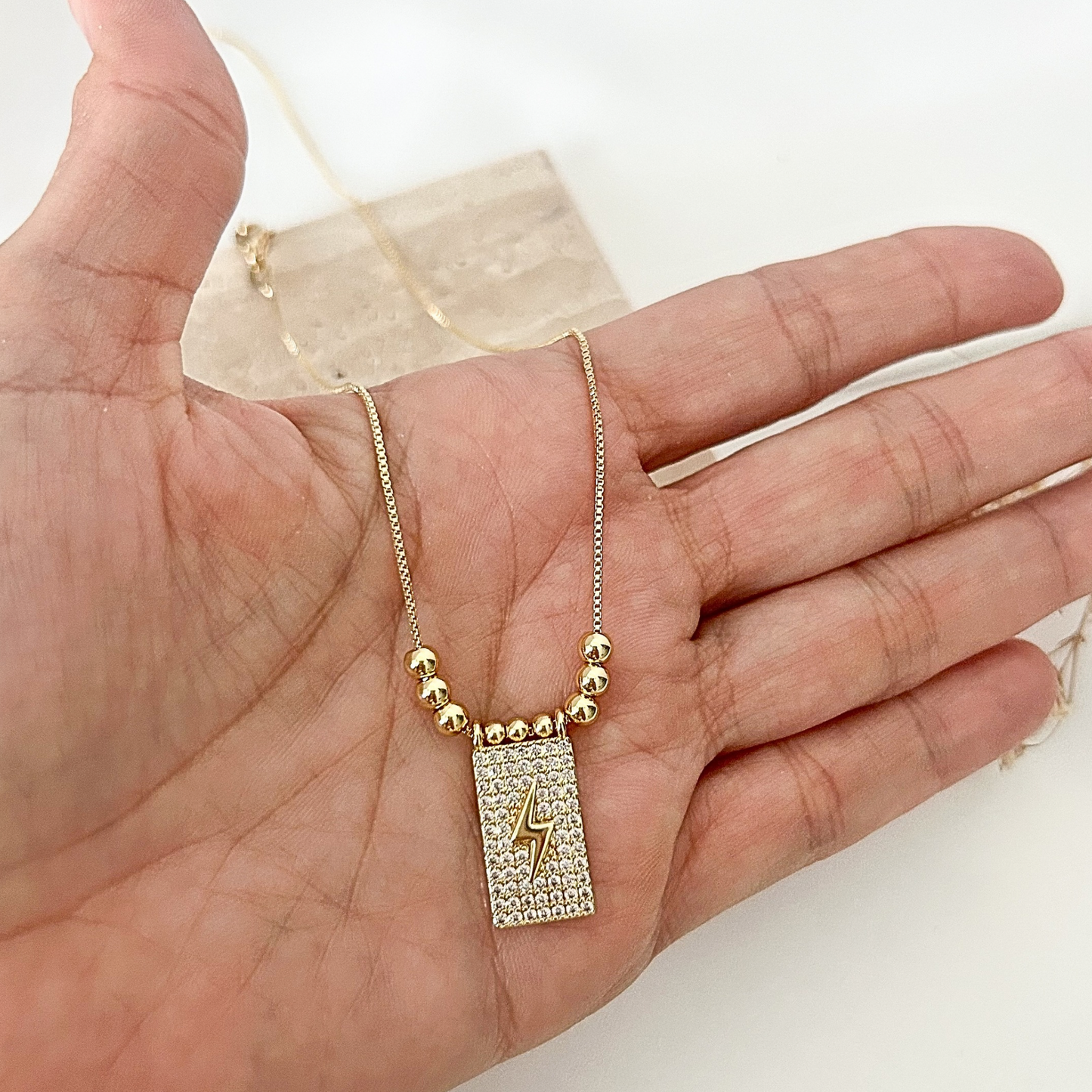 Close-up of a crystal-studded lightning bolt pendant necklace held in hand, showcasing its delicate gold chain and elegant bead details.