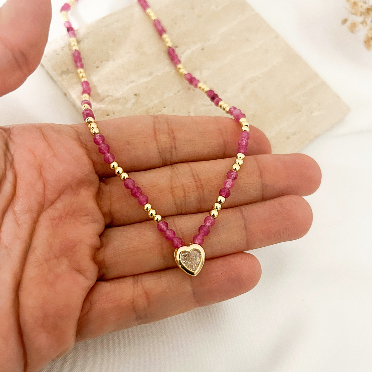 Hand holding pink tourmaline choker to show druzy heart charm detail