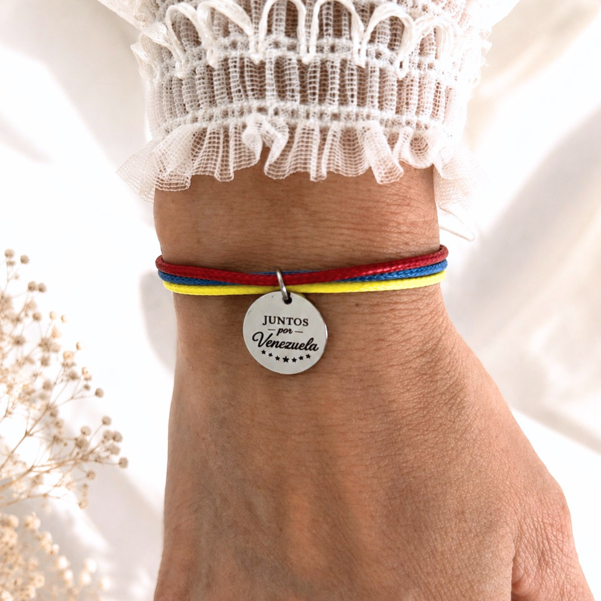 Close-up of an adjustable bracelet in the colors of the Venezuelan flag featuring a stainless steel engraved charm that reads “Juntos por Venezuela.” This handmade charity bracelet supports the purchase of first aid supplies for Venezuela through 100% of the proceeds.