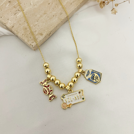 Gold charm necklace with Venezuela license plate, El Chichero, and Toronto candy charms on a stone tray