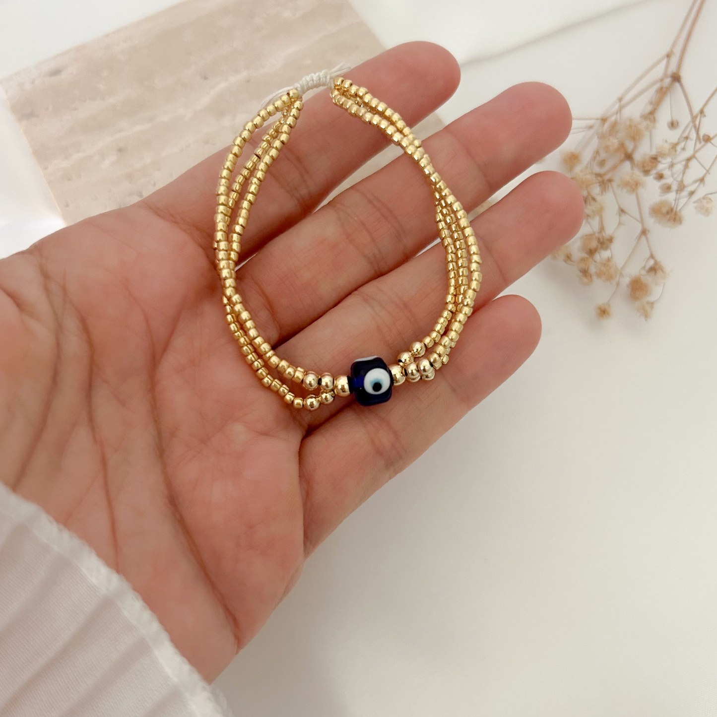 Close-up of a lightweight gold beaded bracelet showcasing a protective evil eye centerpiece and adjustable cord closure.