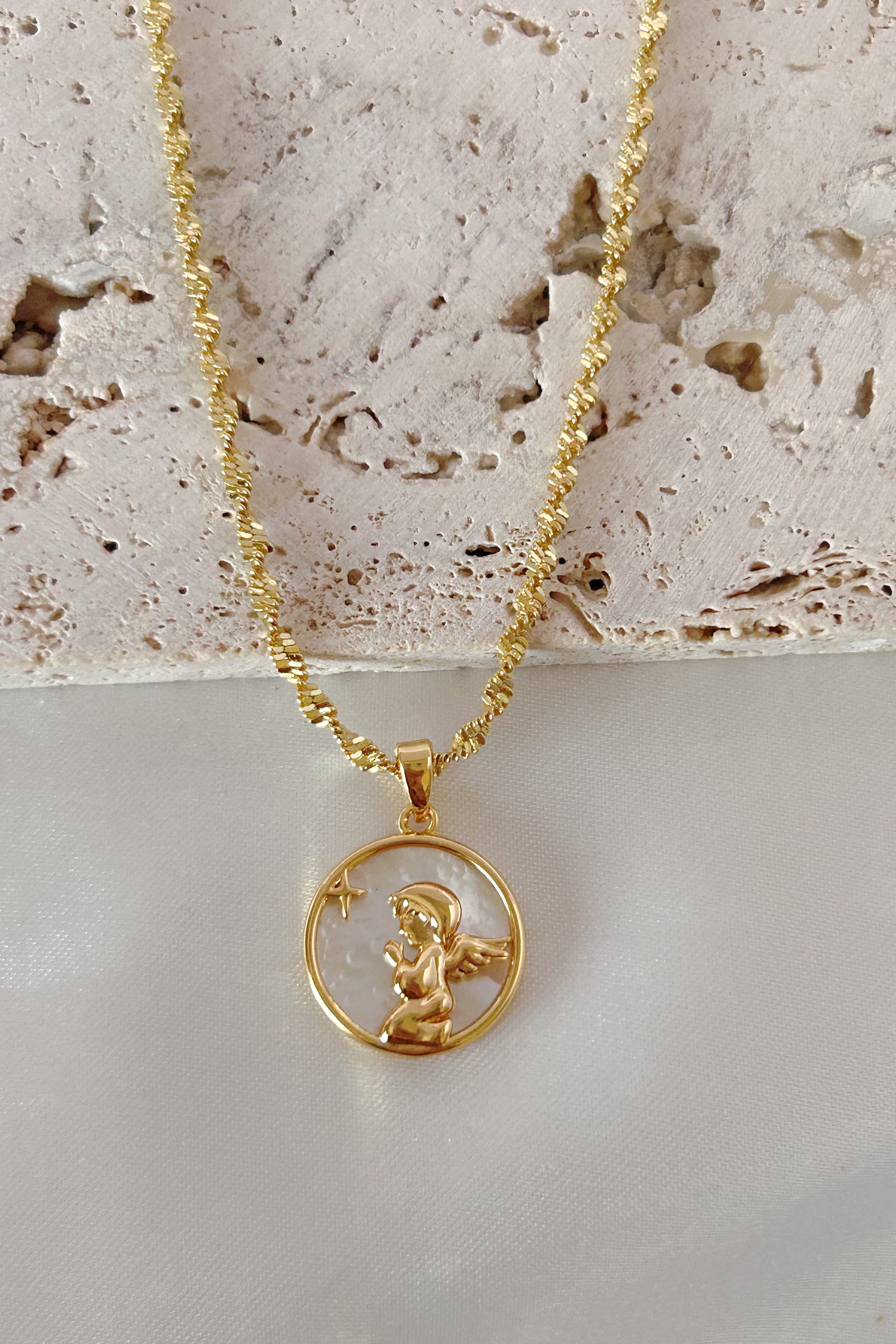 Gold necklace with a pendant featuring a cherub on a textured surface