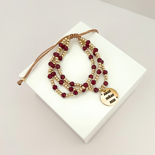 Multi-strand adjustable bracelet featuring burgundy crystal beads, gold-tone accents, and an engraved charm that reads “Amar, Soñar, Reír.”