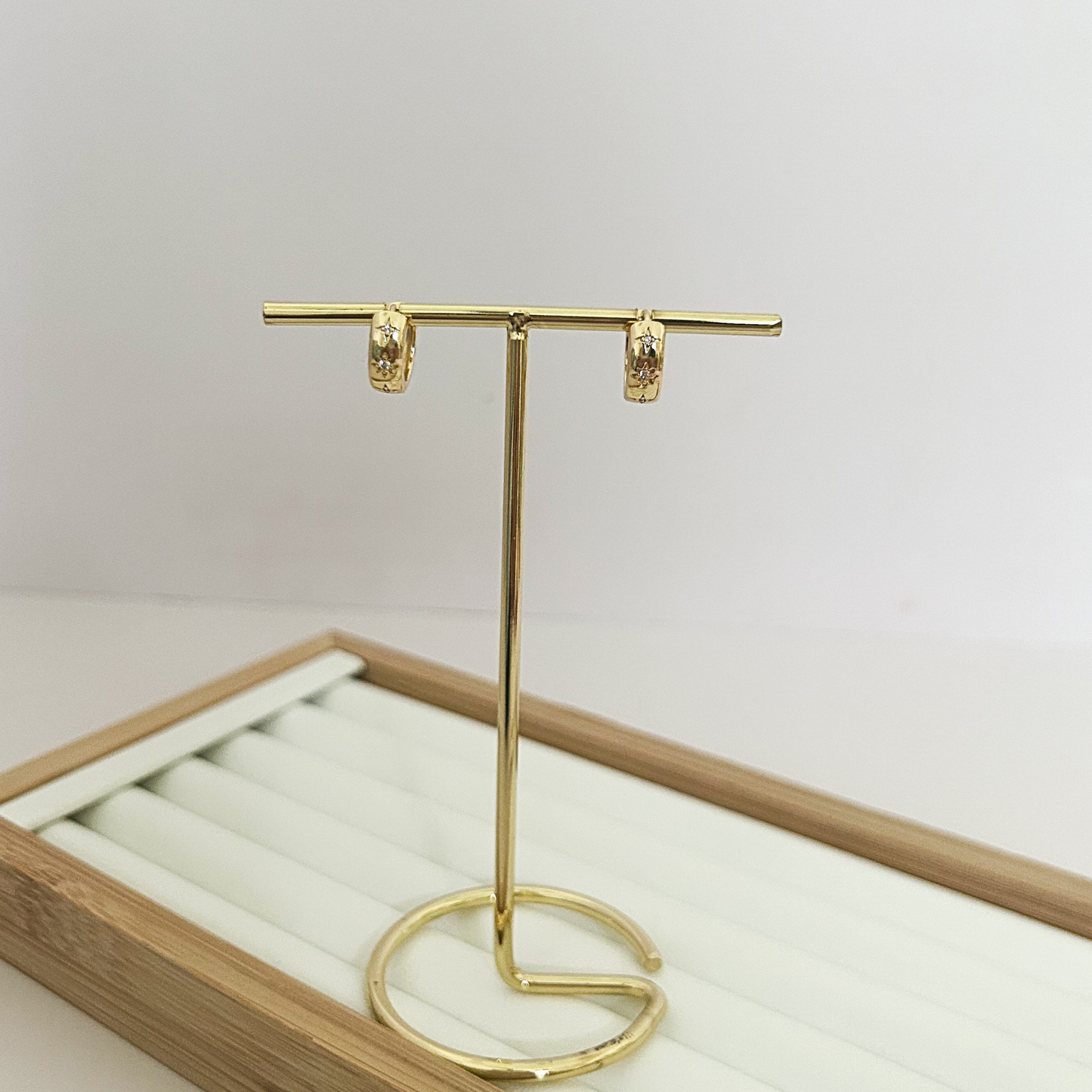 Mini gold star huggie hoop earrings with crystal detail on jewelry stand