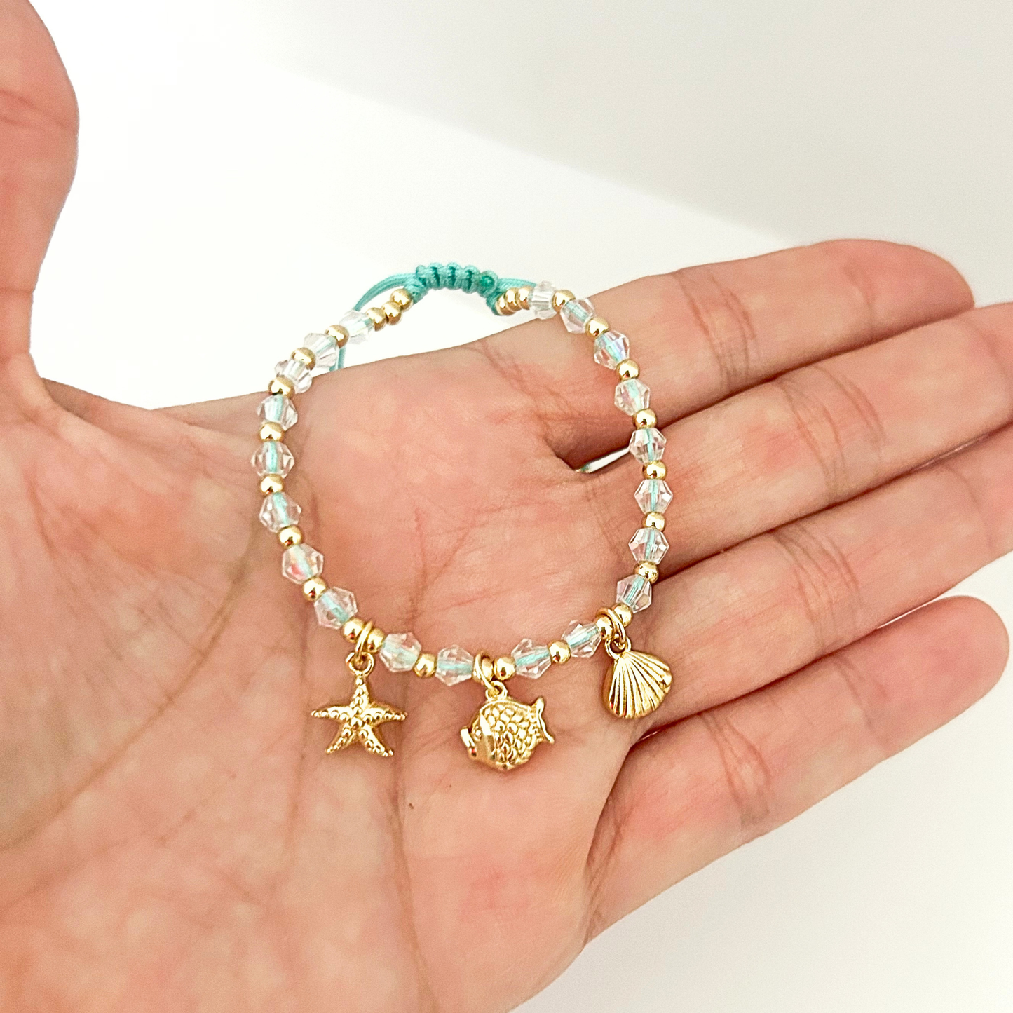 Beach charm bracelet featuring a starfish, fish, and seashell pendant paired with crystal beads and an adjustable turquoise cord.