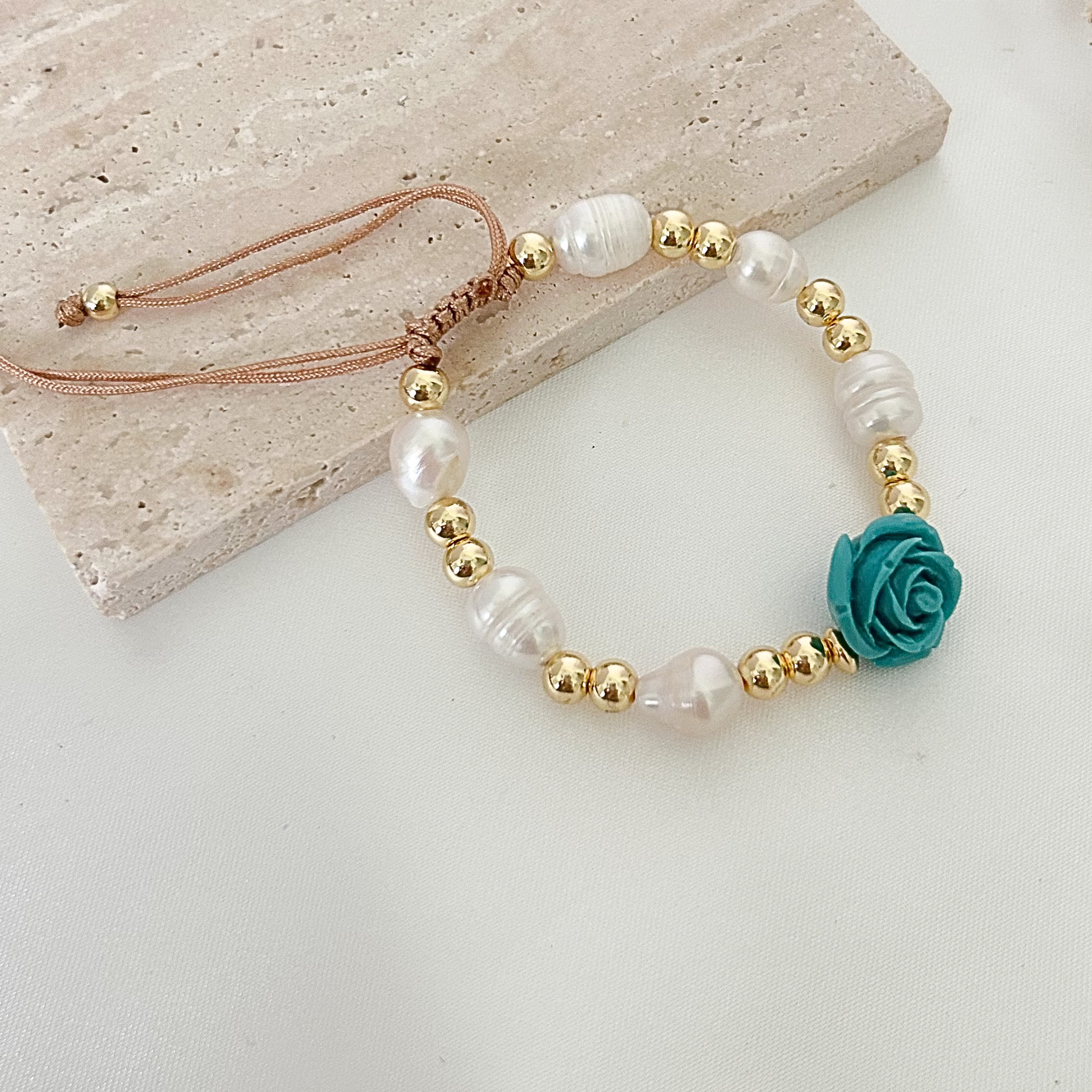 Handcrafted adjustable bracelet with a turquoise floral charm, freshwater pearls, and gold-tone bead details displayed on a light neutral background.