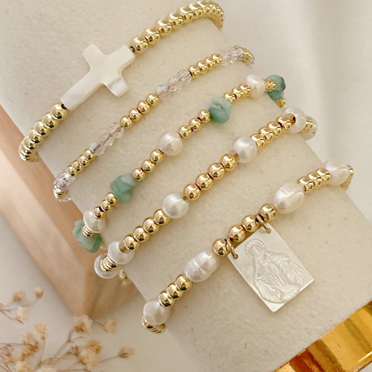 Gold and pearl beaded bracelet with a silver tag on a beige surface.