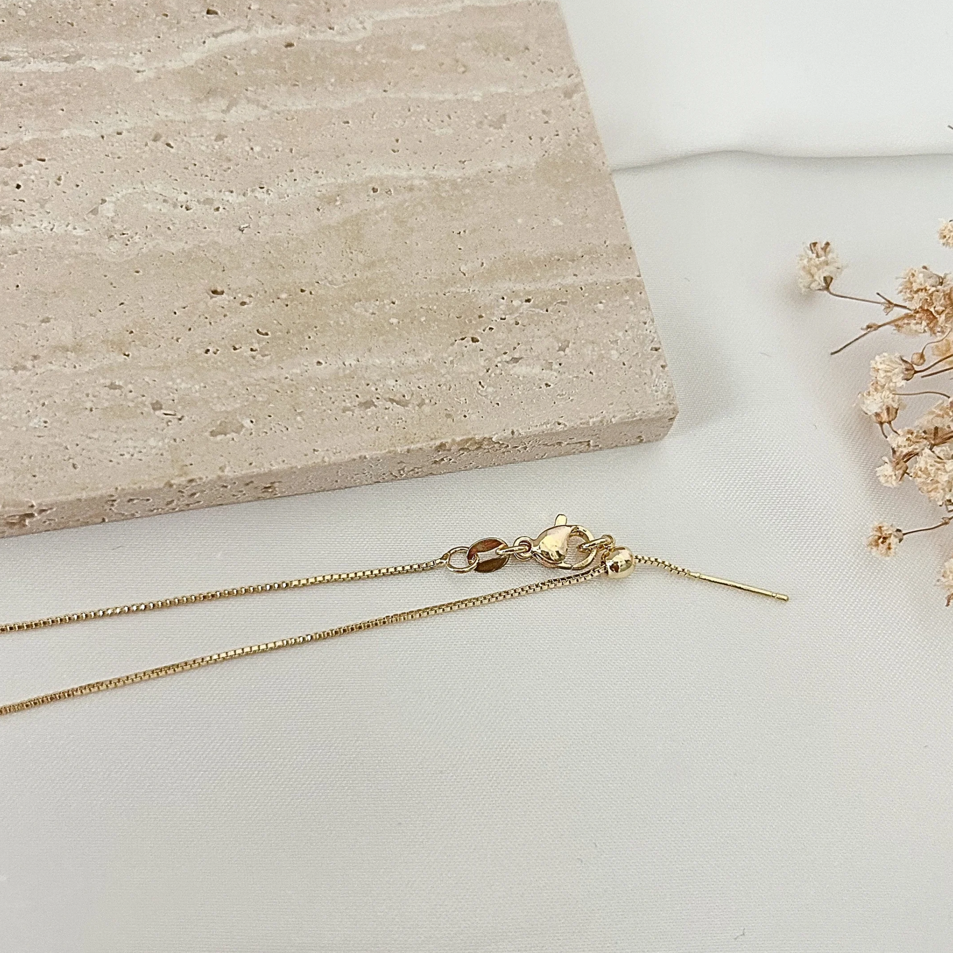 Adjustable gold-tone necklace with a sliding clasp closure and crystal lightning bolt pendant, photographed against a soft neutral background.