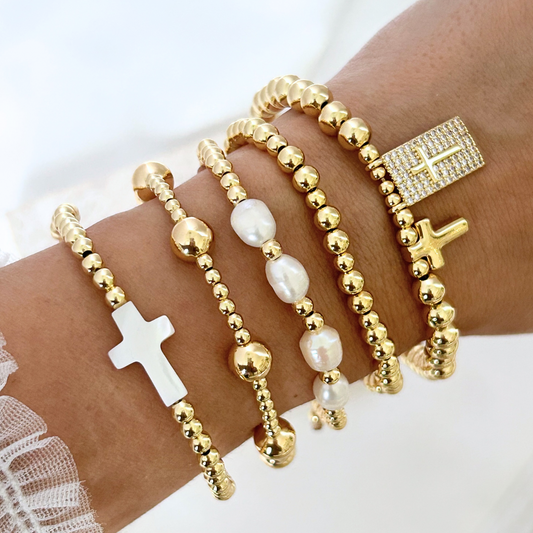 Gold beaded bracelets with cross charms on a wrist against a white background