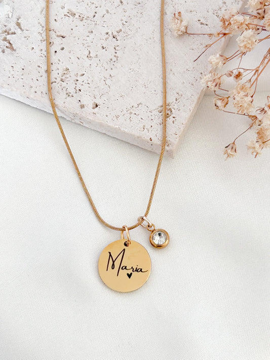 Gold necklace with a round pendant engraved with 'Maria' on a light background
