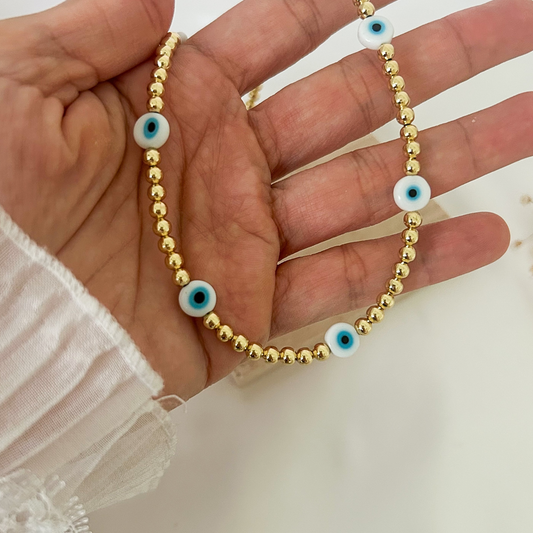 Close-up of a gold-tone beaded necklace accented with protective evil eye beads in white, blue, and black, creating a minimalist yet meaningful everyday accessory.