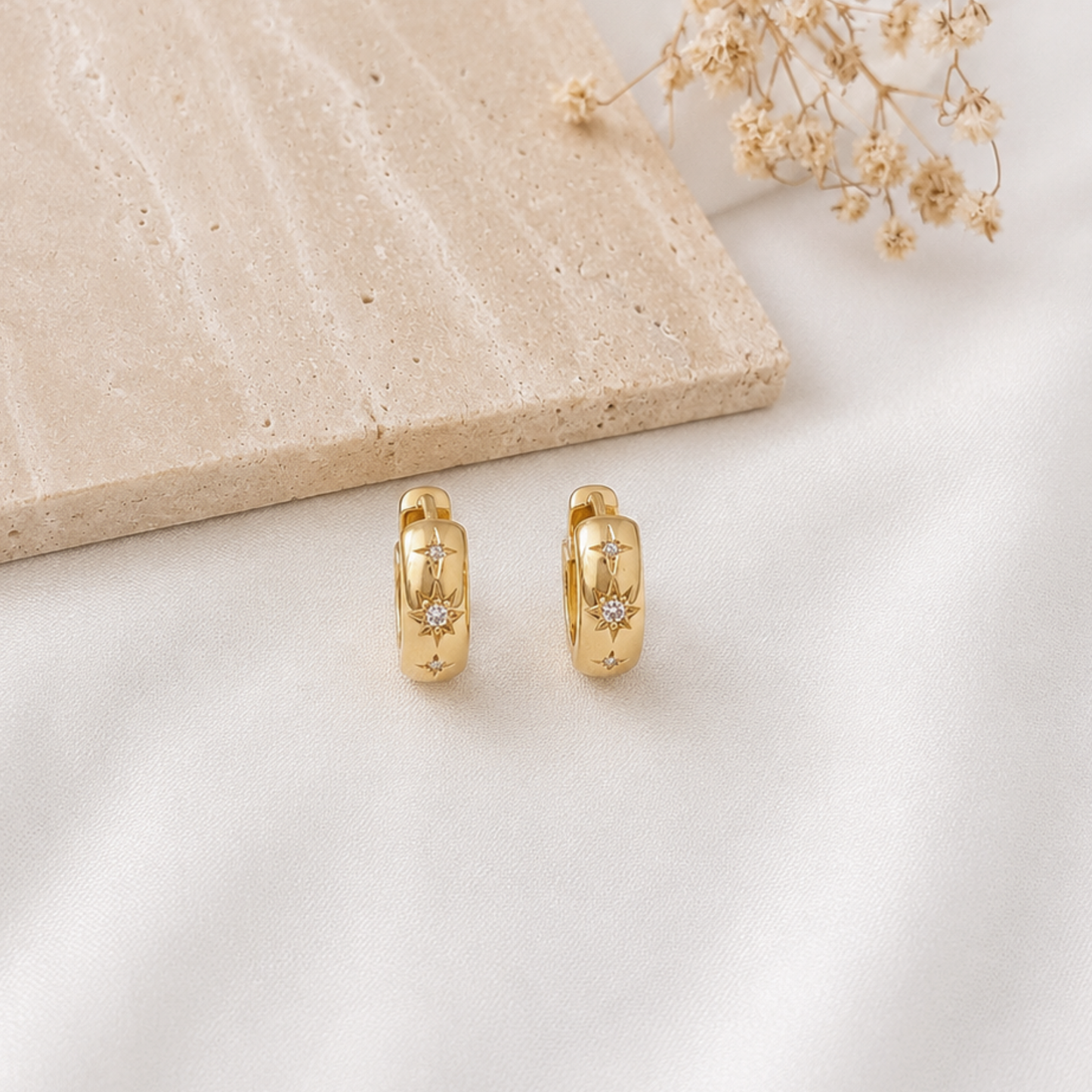 Pair of gold-tone huggie hoop earrings featuring engraved celestial starburst details with sparkling cubic zirconia accents. Minimalist gold hoop earrings with a polished finish and celestial-inspired design, perfect for everyday wear, layering, or gifting.