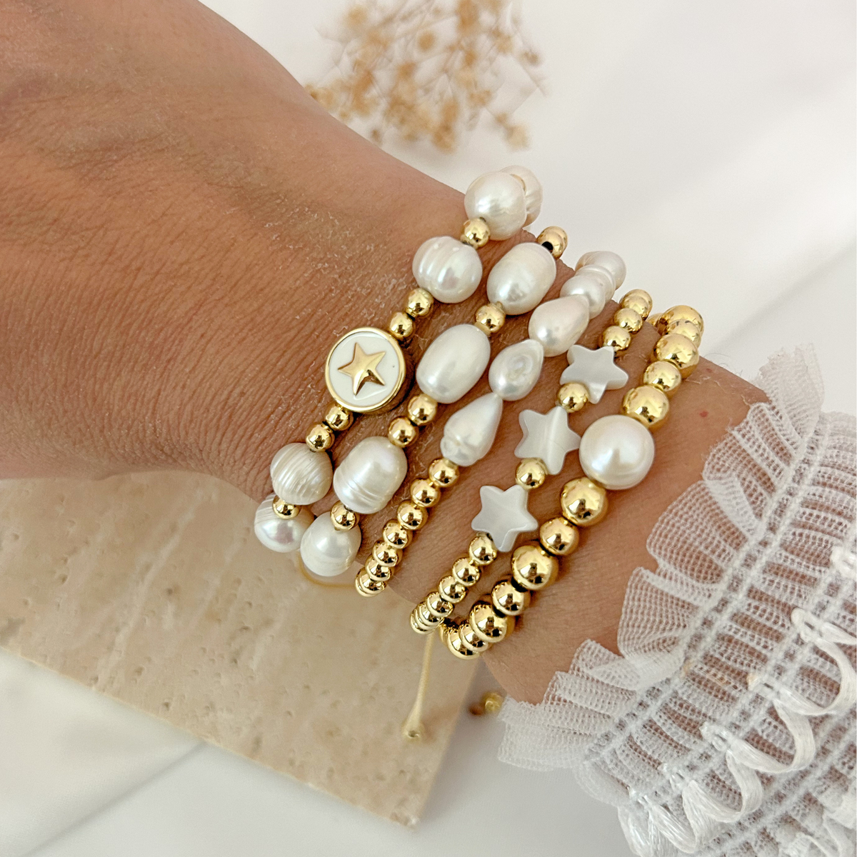 Gold beaded bracelet stack featuring freshwater pearls, white star charms, and a gold star medallion.