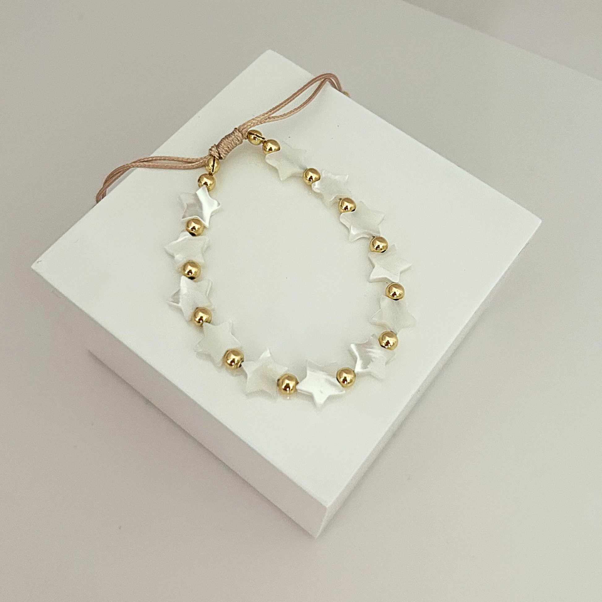 Adjustable bracelet featuring white star-shaped beads and gold-tone accents, creating a delicate and celestial-inspired design.