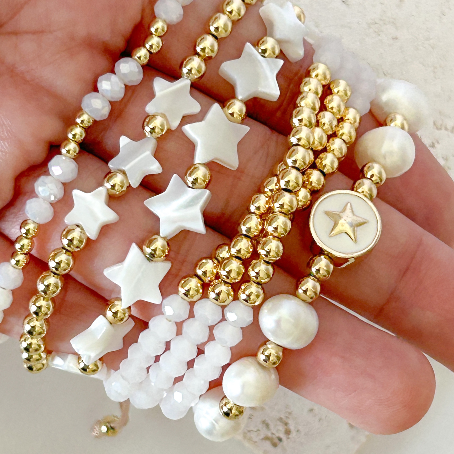 Gold and white beaded bracelets with star-shaped beads on a hand.