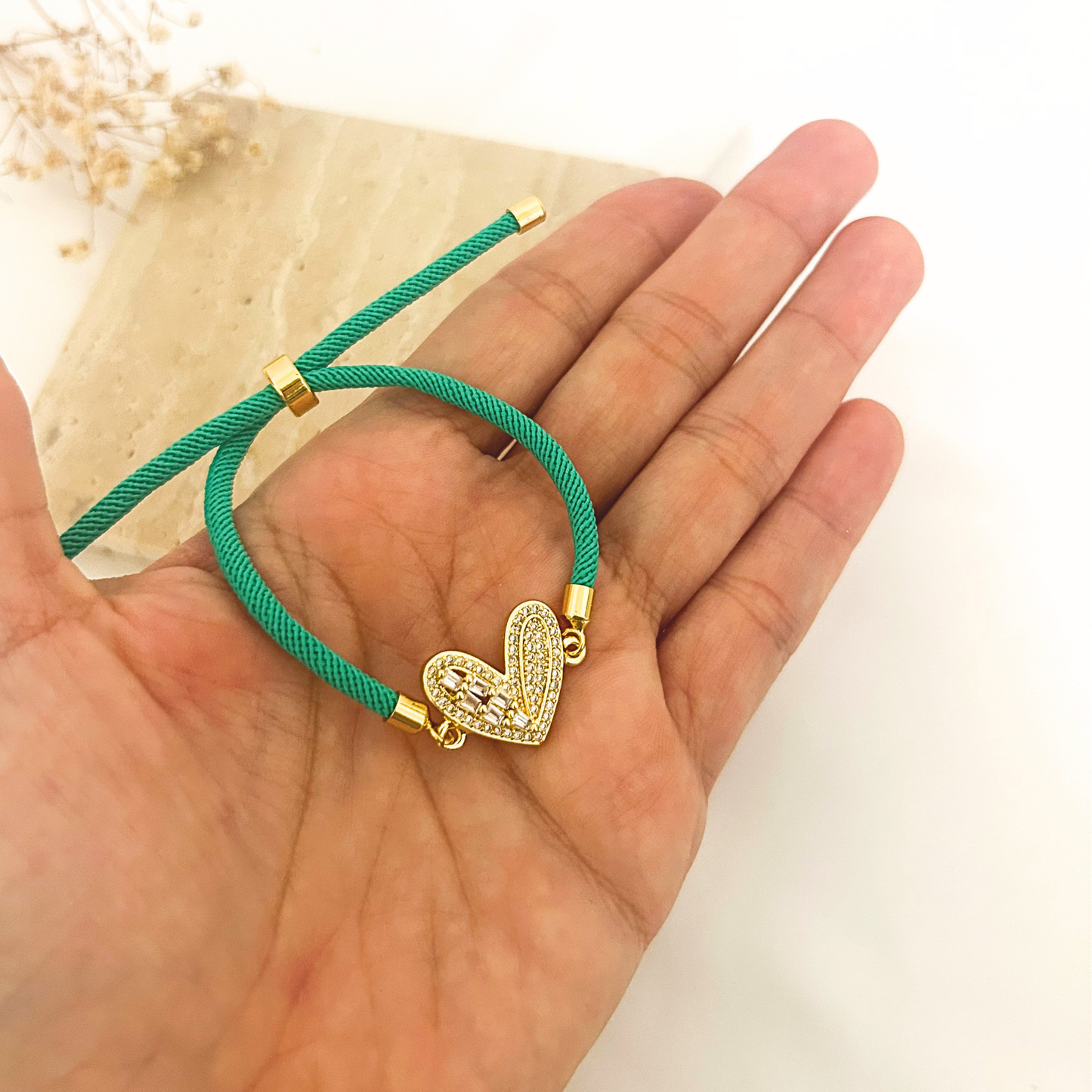 Teal cord bracelet with heart charm held in hand