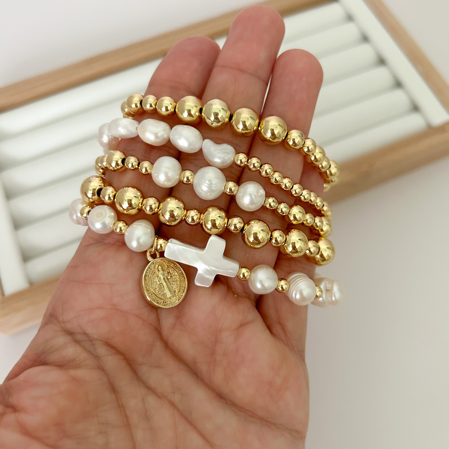 Five gold bracelets with baroque pearls and mother of pearl cross held in hand