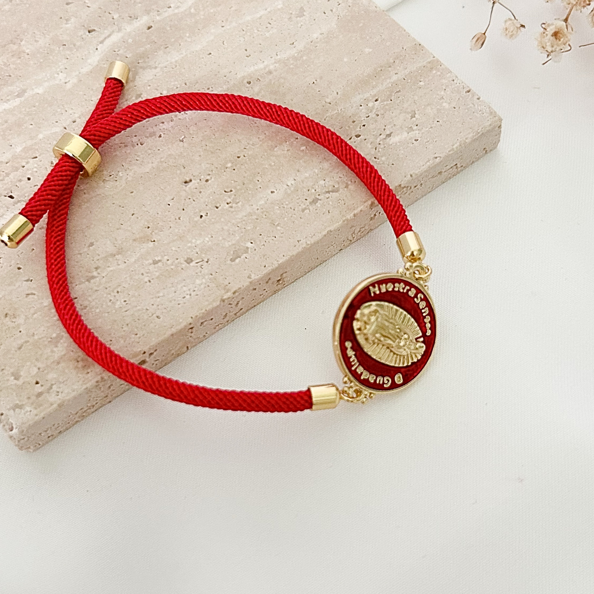 Close-up of a religious bracelet worn on the wrist, showcasing a red cord design and a gold-tone Virgen de Guadalupe medallion, symbolizing faith, protection, and devotion.