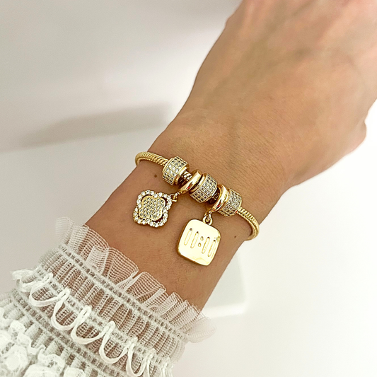 Elegant gold bracelet with crystal-studded charms, including a quatrefoil design and 11:11 pendant, worn on the wrist.
