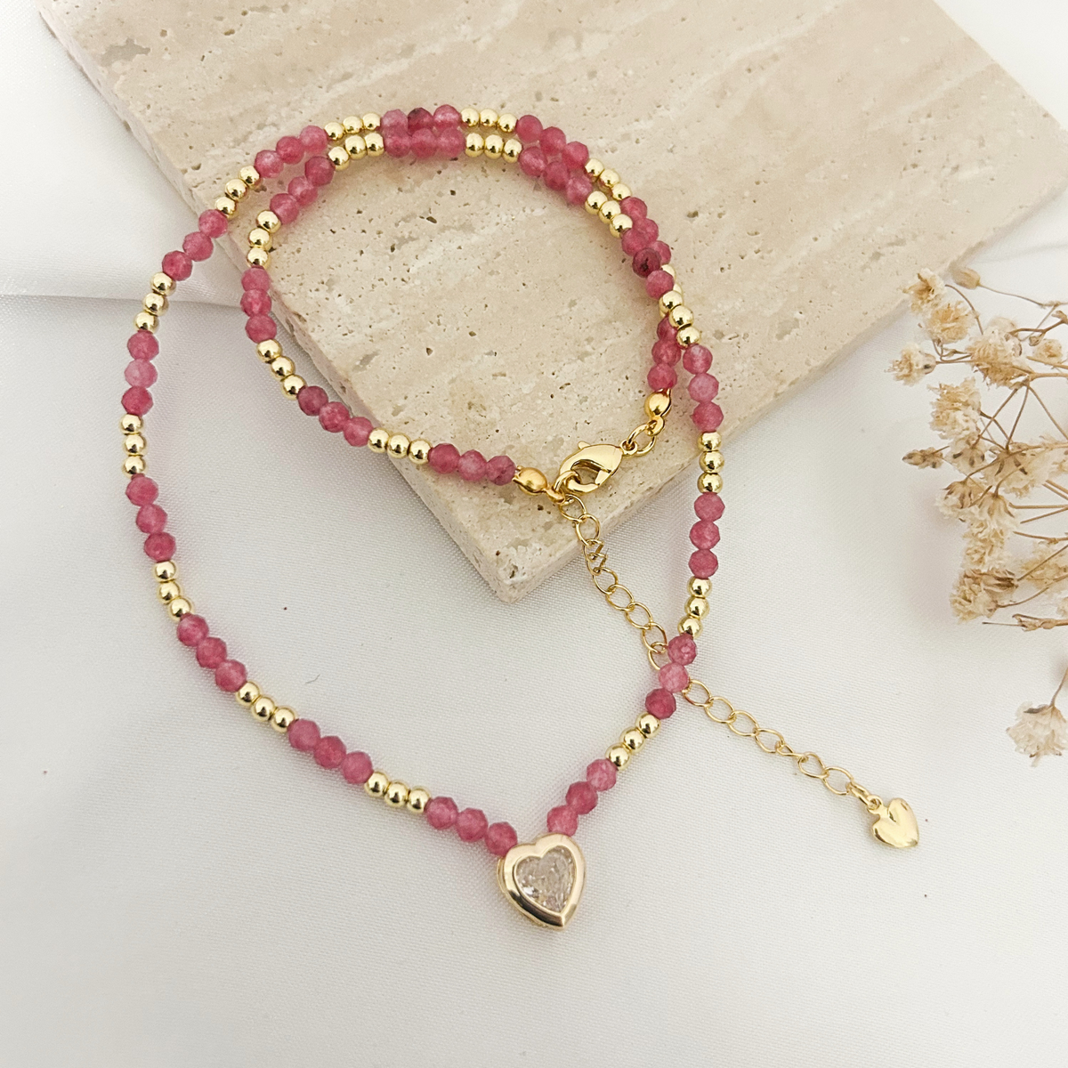 Pink tourmaline beaded choker with druzy heart charm on a stone tray
