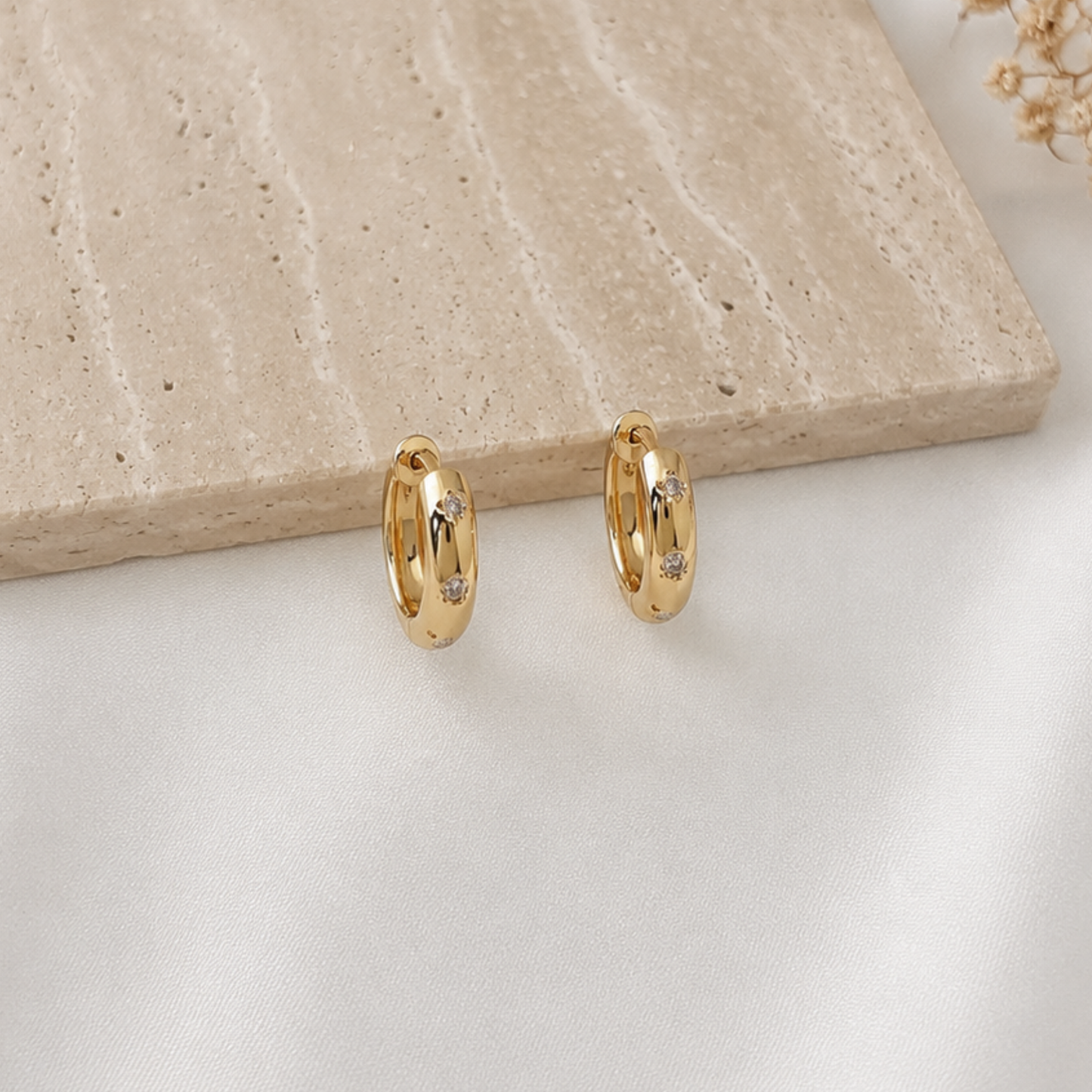 Pair of minimalist gold-tone huggie hoop earrings featuring bezel-set round cubic zirconia accents. Sleek polished gold hoops with subtle sparkle, perfect for everyday wear, stacking with other earrings, or adding an elegant touch to any outfit.