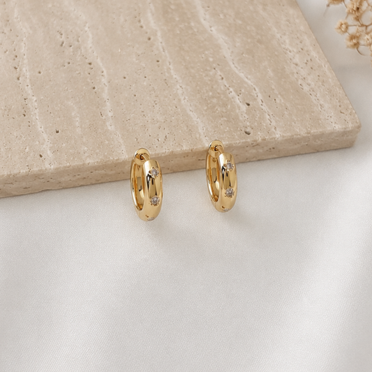 Pair of minimalist gold-tone huggie hoop earrings featuring bezel-set round cubic zirconia accents. Sleek polished gold hoops with subtle sparkle, perfect for everyday wear, stacking with other earrings, or adding an elegant touch to any outfit.