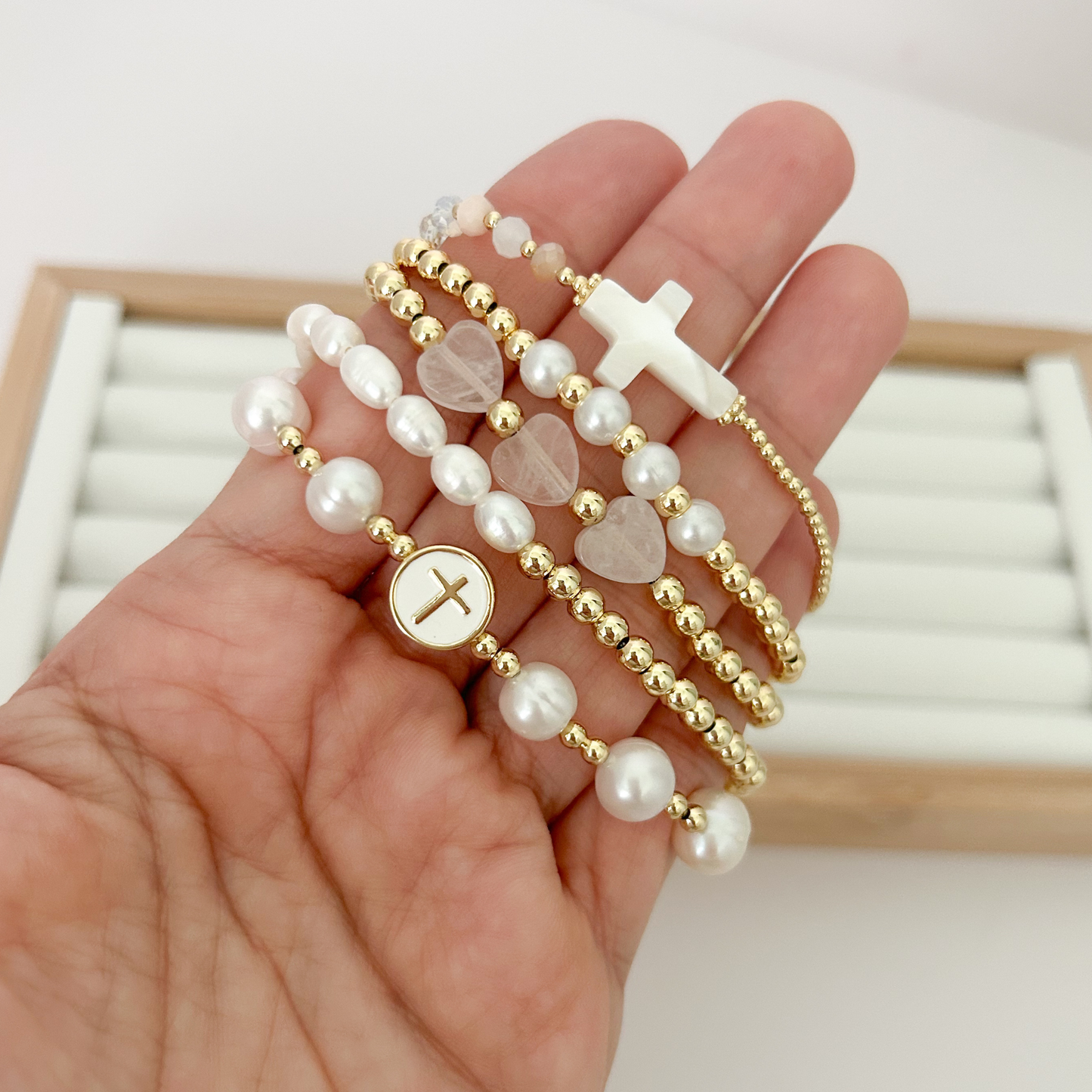 Five gold bracelets with freshwater pearls and cross charms held in hand